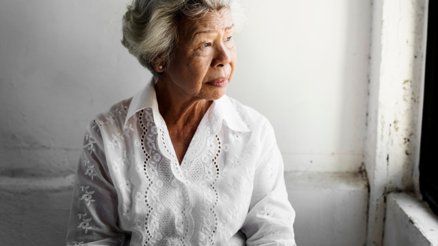 An older woman looking outside of a window