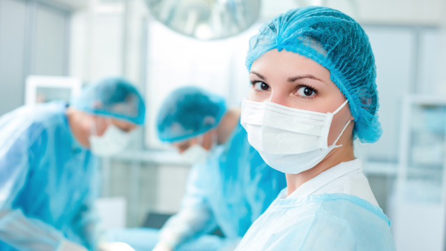Female doctor in operating room, with two male doctors behind her, actively operating
