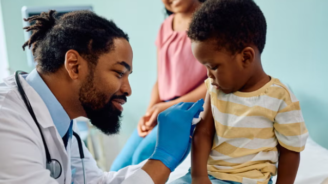 Male doctor putting a bandaid on a little boy sitting in a medical office