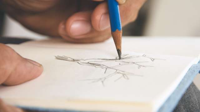 A hand sketches with a pencil on a page in a notebook.