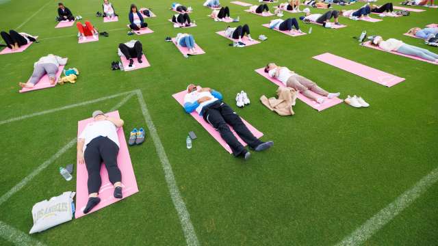Cancer patients and survivors relax on pink yoga mats on the field at the Chargers practice facility