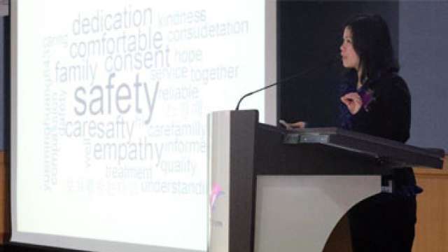 A speaker presents at a podium with a word cloud on a screen behind.