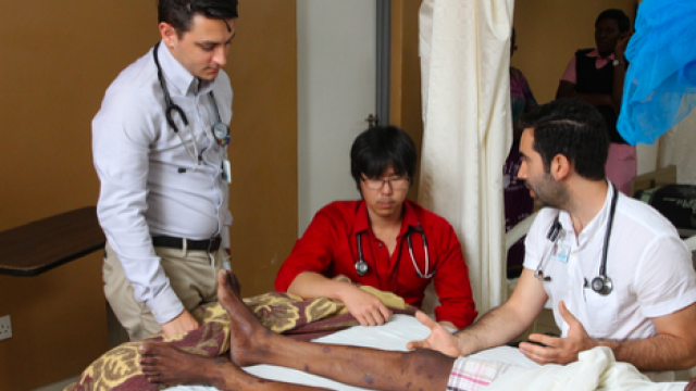 three doctors reviewing a patient's legs in a room