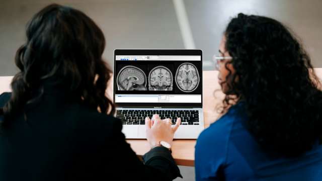  Two people look at a laptop screen showing three brain scans.