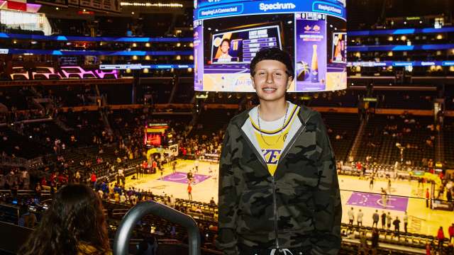 A teen girl poses inside Cyrpto.com Arena with the Lakers court in the background.
