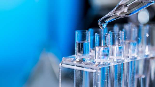 Blue test tubes in lab with pipette dispensing liquid into one tube