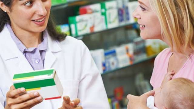 A pharmacist discusses medication with a mother holding a baby in a pharmacy.