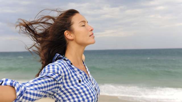 A woman feels the breeze at the beach.