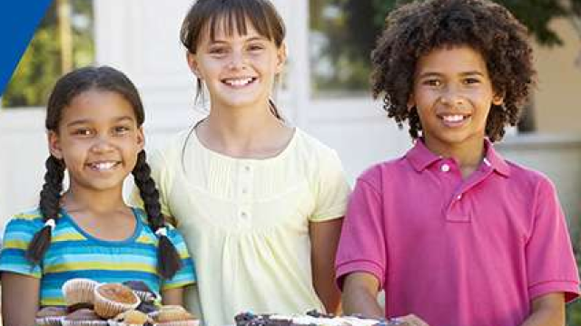 Three children hosting a bake sale with cookies and pastries in front of them.