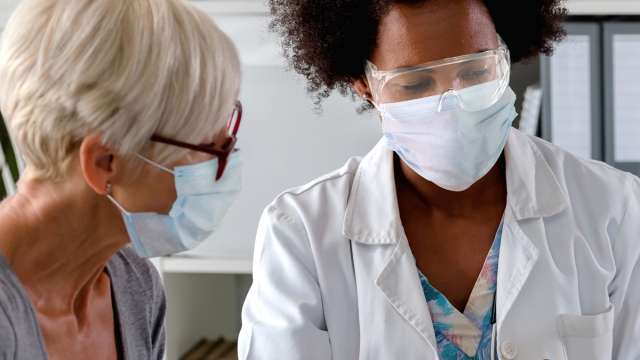 A doctor with a face shield and mask discussing with a masked patient.