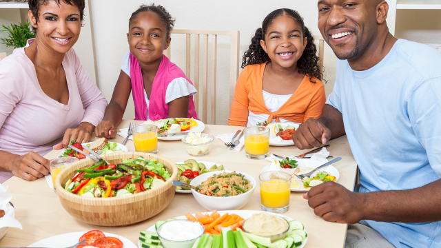 Smiling family enjoys a colorful, healthy meal together at home, promoting balanced nutrition and wellness through shared meals.