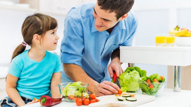 A father and his daughter cutting vegetables in the kitchen while prepping a meal.