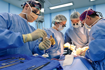 Surgeons in full sterile attire performing a procedure in an operating room, with surgical tools laid out in the foreground.