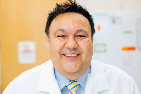 Close-up of Steven Jonas in light blue button-down, yellow and blue tie and white coat.