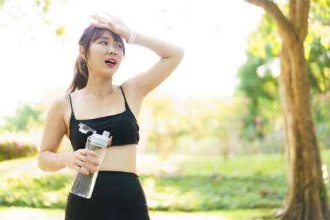 Woman in workout clothes holding water bottle wiping her forehead outdoors