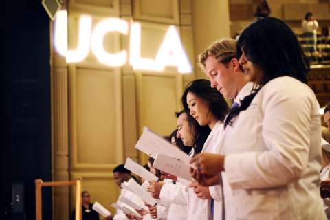 Incoming students of the David Geffen School of Medicine at UCLA read the UCLA Medical Oath to mark the beginning of their medical eduaction. A large logo of UCLA is shown in light in the background.