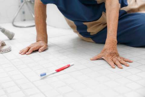 Hands of person on tiled bathroom floor next to toothbrush.