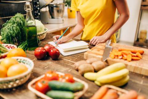 Woman in kitchen taking notes and prepping ingreditents