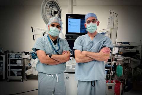 Two surgeons in scrubs and masks standing with arms crossed in an operating room.