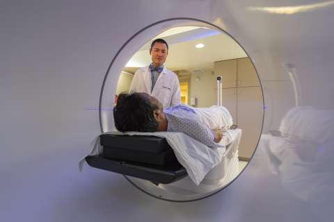 Patient on medical scanner table entering tunnel as technician stands at head.
