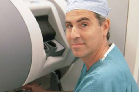 Robert Reiter MD seated at a surgical robot console wearing scrubs and a cap
