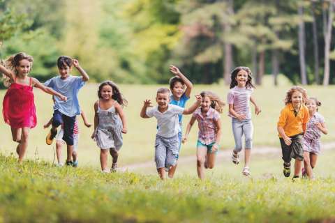 Group of smiling children running toward the camera in a grass field