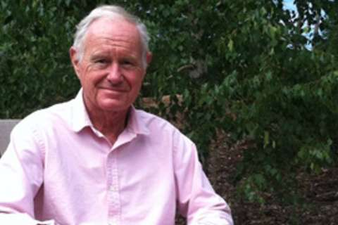 John Hottinger wearing pink shirt seated outdoors against leafy background