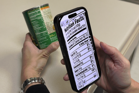 A photo of someone holding a smartphone up to a nutrition label with the label magnified on the screen