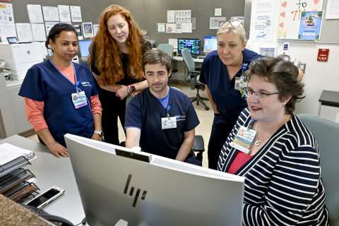 Four healthcare workers and one patient engage around a computer monitor.