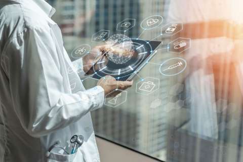 A doctor looks at a handheld computer with high-tech images coming out of it.