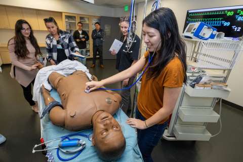 Rita Manukyan, left, Hilary Koenig and a Rosenfeld Hall guest get a close look at the computerized patient simulator in the form of a lifelike manikin.