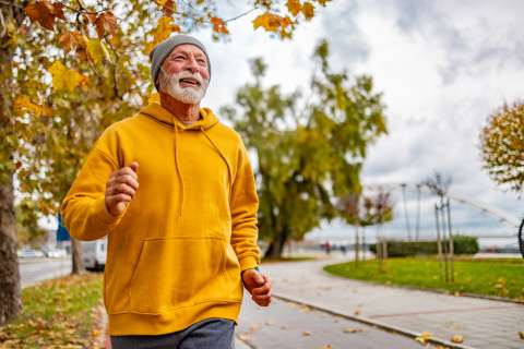 Older man in yellow sweatshirt jogging outside