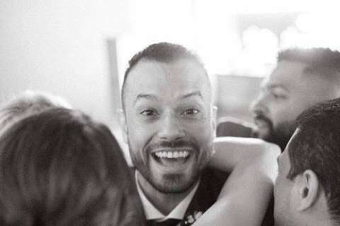 A man with friends and loved ones smiles in a black-and-white photo.