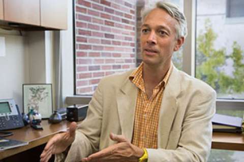 A person gesturing while seated at a desk in an office setting.