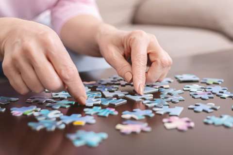 Senior woman playing jigsaw puzzle at home, close up
