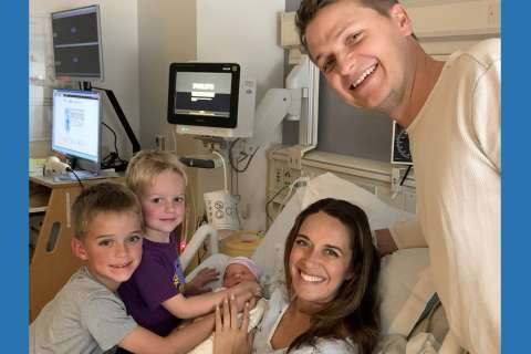 Family gathering around a newborn baby in a hospital room.