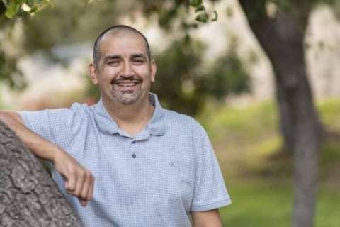 A smiling headshot of Lazaro Barajas, who is leaning on a tree and looking at the camera.