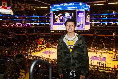 A teen girl poses inside Cyrpto.com Arena with the Lakers court in the background.