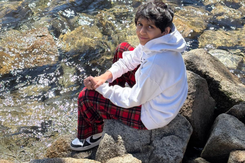 A boy sits on rocks along the water.
