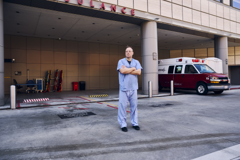 A doctor in scrubs stands in front of the ER.