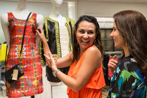 Three women in a boutique; smiling woman shows a bracelet to a friend.
