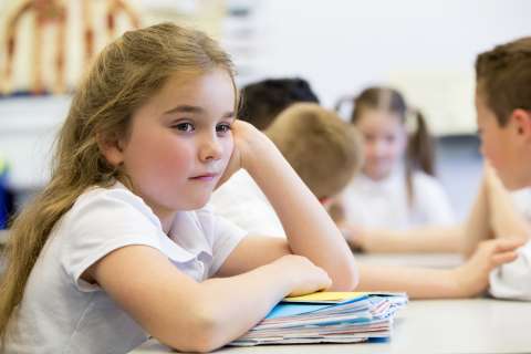Young girl leans on her hand and looks away from her classmates.