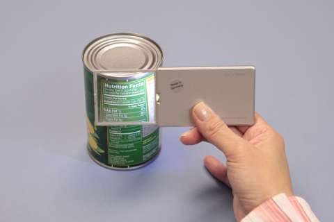 A hand holding a physical magnifier up to a can 