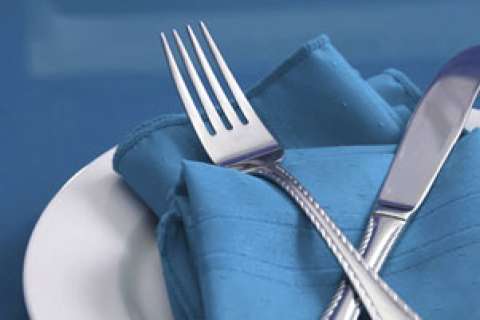 Silverware resting on a blue napkin placed on a white plate.