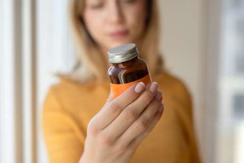 Person holding small amber medicine bottle with white cap