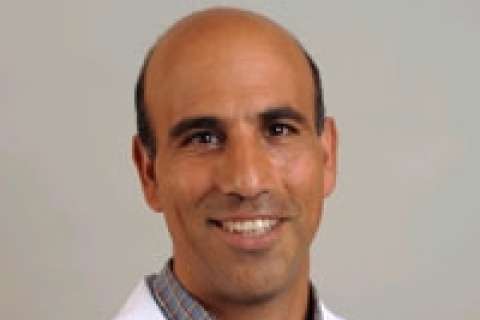  A headshot of Dr. Robert Ashley, a bald man with dark eyes and a warm smile, wearing a collared shirt under a white lab coat.