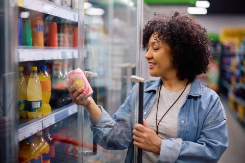Woman in grocery aisle holding a jar and reading its label