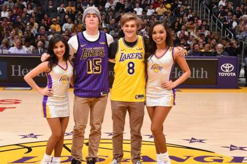 Two people wearing Los Angeles Lakers jerseys posing with two Lakers cheerleaders on the basketball court during a game.
