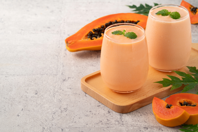 Two papaya milks in glasses with halved papaya and mint garnish