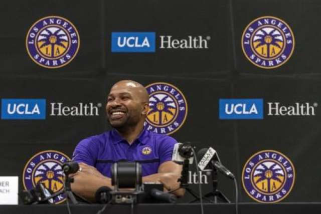 A headshot of the smiling LA Sparks GM and Head Coach, a man with a shaved head and beard, wearing a purple shirt at a press conference.
